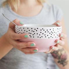 a woman holding a pink and white bowl with polka dots on the side, while holding a spoon in her hand