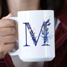 a woman holding a coffee mug with the letter m painted on it