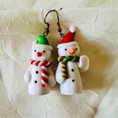 two snowmen wearing christmas hats and scarfs are hanging from ear hooks on a white sheet