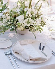 a white table setting with flowers and silverware