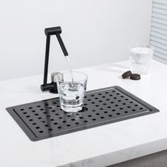 a glass filled with water sitting on top of a white counter next to a black faucet