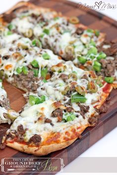 a pizza with meat, cheese and green peppers on a wooden cutting board in front of a white background