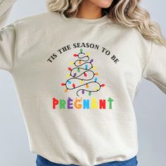 a woman wearing a white christmas sweater that says tis the season to be pregnant