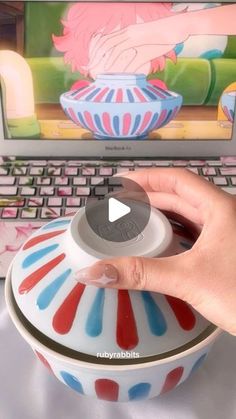 a person using a laptop computer with a colorful bowl on the keyboard and an image of a woman's hand