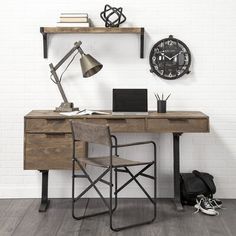 a desk with a chair, laptop and lamp on it in front of a white brick wall