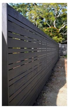 the side of a black fence with wooden slats on it and trees in the background