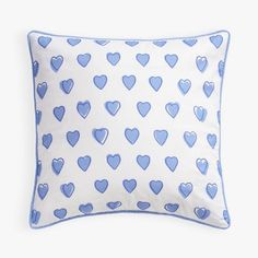 a blue and white pillow with hearts printed on the front, sitting on a white surface