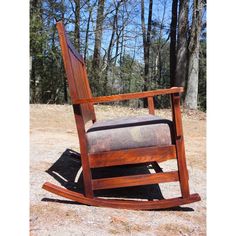 a wooden rocking chair sitting on top of a dirt field in front of some trees