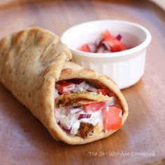 a pita with meat and vegetables on it next to a small bowl of dip