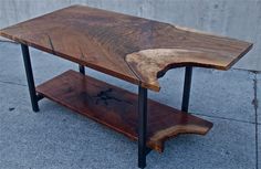 a wooden table sitting on top of a sidewalk next to a cement wall with black metal legs