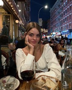 a woman sitting at a table with a glass of wine and bread in front of her