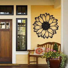 a wooden bench sitting in front of a yellow house with a large sunflower on the wall