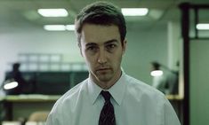 a man wearing a white shirt and tie standing in an office setting with his hands on his hips