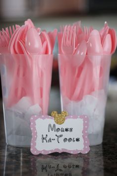 pink plastic utensils in clear cups with name tag on top for guests to use