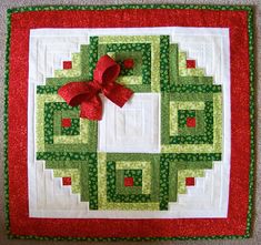 a green and red quilted wall hanging with a bow on the center, in front of a white background