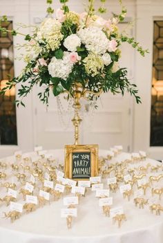 a table topped with a vase filled with white flowers and place cards on top of it