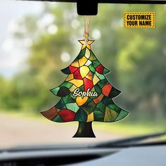 a stained glass christmas tree ornament hanging from a car's dashboard window