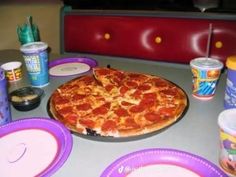 a pizza sitting on top of a table next to plastic plates and cups filled with condiments