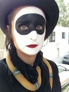 a woman with black and white face paint on her face wearing a hat, scarves and scarf