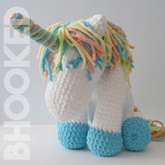 a crocheted stuffed unicorn with multicolored manes and tail sitting on a white surface