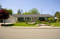 a house that is sitting on the side of a road with trees and bushes in front of it