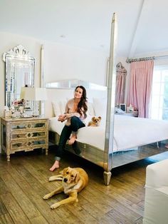 a woman sitting on top of a bed next to a dog laying on the floor