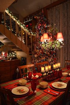 a dining room table set for christmas dinner with lit candles in front of the tree