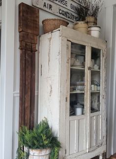 an old white cabinet sitting in the corner of a room next to a potted plant