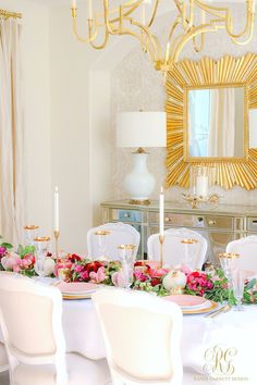 the table is set with white chairs and pink flowers in front of a gold mirror