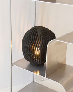 a black vase sitting on top of a shelf next to a metal object with flames coming out of it