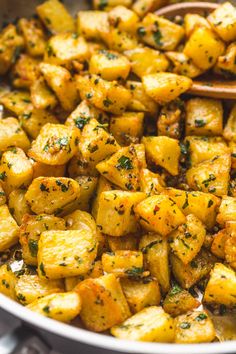 cooked potatoes in a pan with a wooden spoon on the side and herbs sprinkled on top