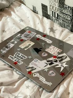 an open laptop computer sitting on top of a white bed covered in paper and stickers