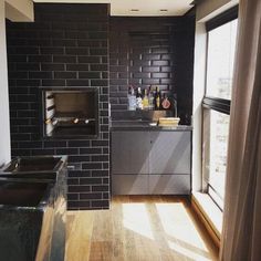 a kitchen with black brick walls and wood flooring next to an open fire place