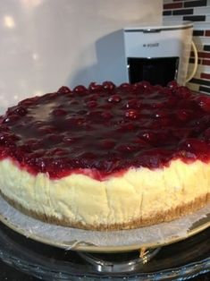 a cheesecake with blueberry topping on a glass cake plate in front of a microwave