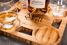 a bottle of whiskey sitting on top of a wooden tray next to two glass glasses