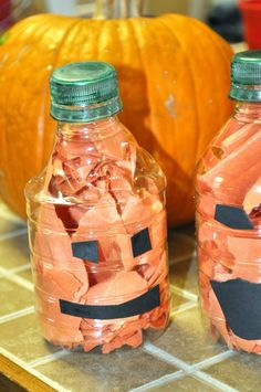 two glass bottles filled with candy sitting on top of a counter next to pumpkins