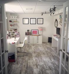 an office with white desks and shelves filled with personal items on the wall, along with open doors leading to another room