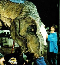 an adult dinosaur is being held up by two men in front of him and another man standing next to it