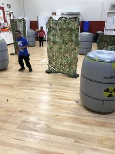 a young boy is playing in an exercise room with barrels and trash cans on the floor