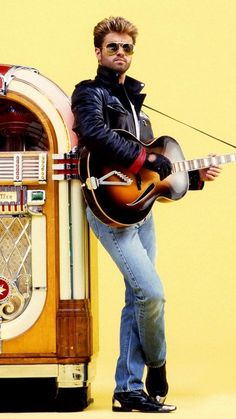 a man holding an electric guitar standing next to a jukebox with a radio on it