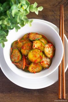 a white bowl filled with food next to chopsticks and a plant in the background