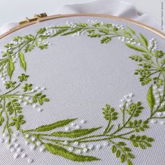 a close up of a embroidery on a piece of cloth with green leaves and white flowers