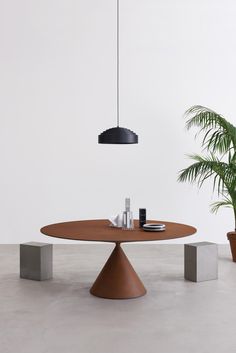 a round wooden table sitting next to two potted plants