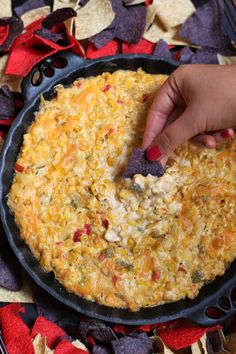 a person dipping tortilla chips into a skillet filled with cheese and vegetables