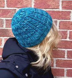 a woman wearing a blue knitted hat against a brick wall with her back to the camera