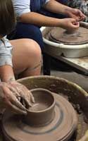 two women are making clay pots on the potter's wheel