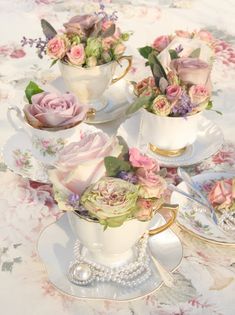 three tea cups with flowers in them sitting on a tableclothed table cloth,