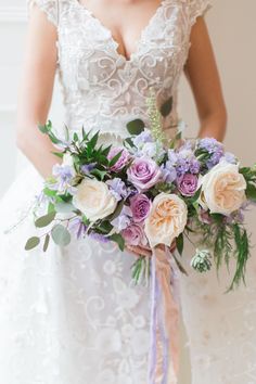 a bride holding a bouquet of flowers in her hand and wearing a wedding dress with lace