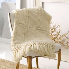 a white chair with a crocheted blanket on it's back and legs