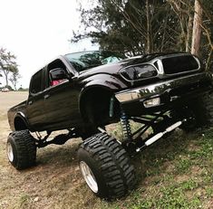 a large black truck parked on top of a grass covered field next to some trees